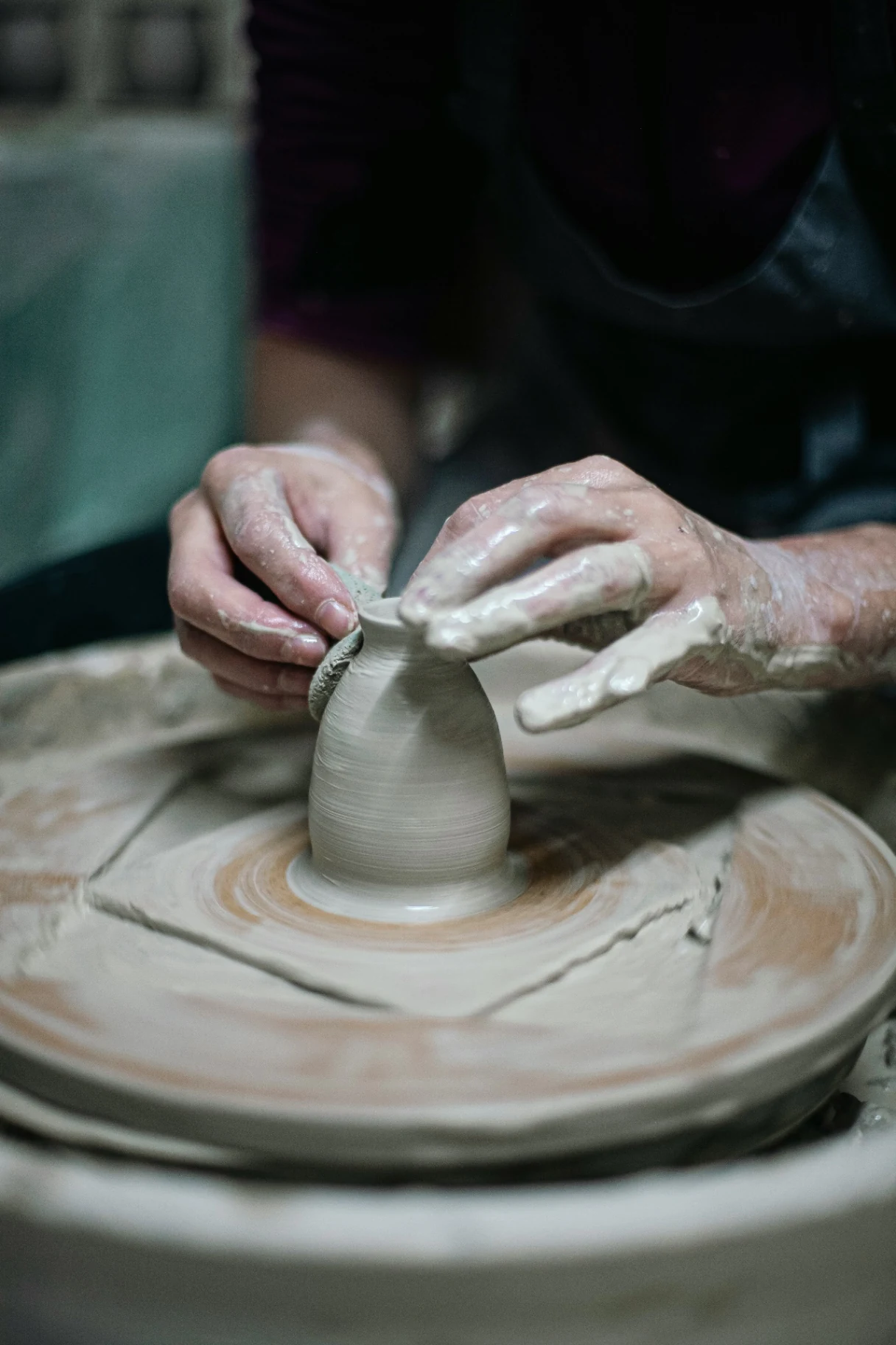 Hands shaping a clay vessel on a pottery wheel